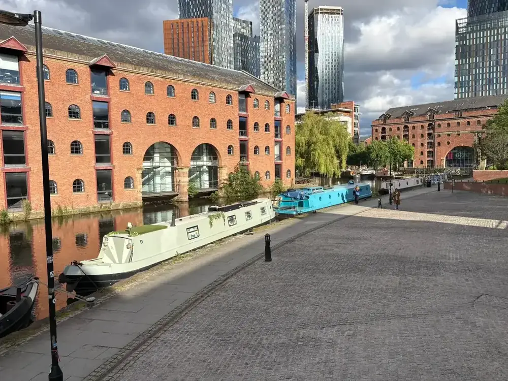 Narrowboats moored at Castlefield basin in Manchester, with the city skyline rising behind